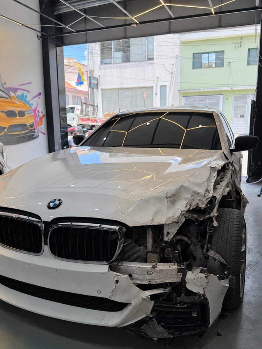 BMW Série 5 branco com a dianteira direita destruída após colisão, na entrada da All In Garage